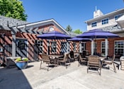 Thumbnail 3 of 22 - A patio with chairs and umbrellas is set against a brick building.