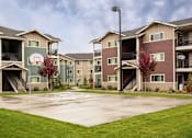 Thumbnail 2 of 8 - A basketball court is in the middle of a grassy area in front of apartment buildings.