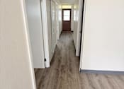 Thumbnail 15 of 15 - A long hallway with white walls and wood flooring.