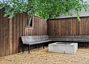 Thumbnail 5 of 32 - A bench sits in front of a wooden fence with a concrete fire pit in front of it.
