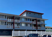 Thumbnail 2 of 20 - A grey building with a red roof and white fence.