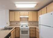 Thumbnail 6 of 6 - A kitchen with a white refrigerator, sink, and stove.