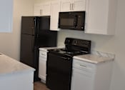 Thumbnail 11 of 19 - Hampton Court Apartments kitchen cabinets, stove, microwave, and refrigerator