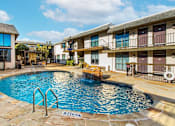 Thumbnail 9 of 41 - A swimming pool in front of a building with a stone border.