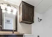 Thumbnail 35 of 41 - A white toilet sits in a bathroom with a wooden cabinet and a mirror above it.