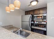 Thumbnail 29 of 41 - A kitchen with a stainless steel refrigerator and oven, a sink, and three hanging lights.