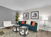 Thumbnail 36 of 53 - A living room with a green couch, a white chair, and a glass table.
