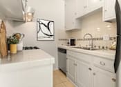 Thumbnail 4 of 13 - A white kitchen with a black fridge and a white stove.
