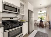 Thumbnail 1 of 25 - A modern kitchen with white appliances and a dining area with a table and chairs.