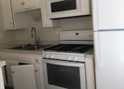 Thumbnail 5 of 21 - A white kitchen with a stove, oven, microwave, and refrigerator.
