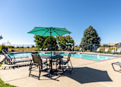Thumbnail 7 of 33 - A table with chairs and an umbrella is set up by a pool.