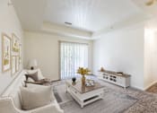 Thumbnail 18 of 33 - A living room with a white couch, a coffee table, and a window with blinds.