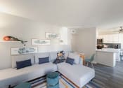 Thumbnail 9 of 24 - a living room with a couch and a table with a kitchen in the background