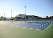 Thumbnail 29 of 35 - A tennis court with a building in the background.