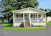 Thumbnail 1 of 3 - A small white house with a porch and a red door.