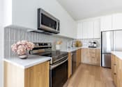 Thumbnail 64 of 67 - A modern kitchen with wooden cabinets and a black microwave above the stove.