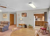 Thumbnail 8 of 14 - a living room with a wooden table and chairs and a kitchen in the background