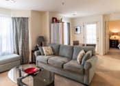 Thumbnail 6 of 20 - A living room with a grey couch and a glass coffee table.