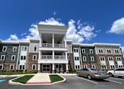 Thumbnail 1 of 19 - A large apartment complex with a car parked in front.