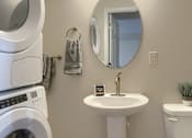 Thumbnail 38 of 48 - A white washing machine sits next to a white pedestal sink in a small bathroom.