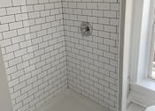 Thumbnail 6 of 13 - A white tiled shower with a drain in the middle.