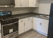 Thumbnail 9 of 13 - A kitchen with white cabinets and a black refrigerator.