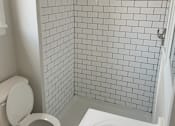 Thumbnail 4 of 13 - A white toilet sits next to a white sink in a white tiled bathroom.