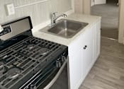 Thumbnail 10 of 13 - A kitchen with a stove, sink and cabinets.