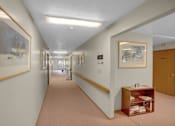 Thumbnail 10 of 14 - a long corridor with paintings on the walls and a small shelf with books