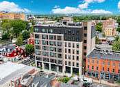 Thumbnail 44 of 73 - A modern building with a flat roof is surrounded by other buildings.