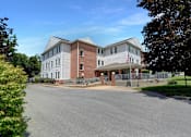 Thumbnail 1 of 16 - Apartments in Three Springs | Three Springs Estates | a large brick building with a gray roof and a black asphalt road in front of it