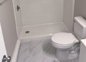 Thumbnail 18 of 23 - A white toilet in a small bathroom with a walk-in shower.