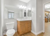 Thumbnail 12 of 30 - A white toilet is in a bathroom with a wooden cabinet and a mirror above the sink.