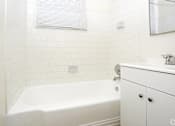 Thumbnail 6 of 47 - A white bathroom with a tub, sink, and mirror.