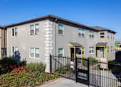 Thumbnail 24 of 47 - A grey building with a black fence and gate in front.