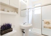 Thumbnail 20 of 30 - A white bathroom with a white sink and a white towel hanging on the shower door.