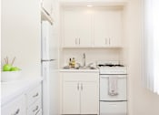 Thumbnail 13 of 30 - A white kitchen with a refrigerator, sink, and stove.
