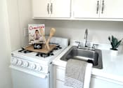 Thumbnail 14 of 30 - A white kitchen with a stove and sink.