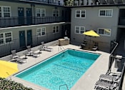 Thumbnail 22 of 30 - A swimming pool is surrounded by chairs and a building.