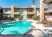 Thumbnail 16 of 37 - A pool surrounded by a patio with chairs and a building in the background.