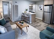 Thumbnail 1 of 49 - A modern living room with a grey sofa, a wooden coffee table, and a kitchen area in the background.