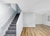 Thumbnail 14 of 34 - A staircase with a grey carpeted runner leads up to a white wall.