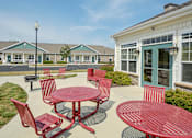 Thumbnail 4 of 23 - A red table and chairs are set up outside a building.