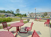 Thumbnail 9 of 23 - A sunny day at a park with red chairs and tables.