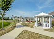 Thumbnail 8 of 23 - A white gazebo is surrounded by a paved walkway in a grassy area.