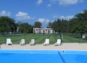 Thumbnail 2 of 9 - A pool with chairs around it and a building in the background.