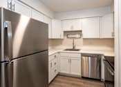 Thumbnail 3 of 9 - A kitchen with a stainless steel refrigerator and white cabinets.