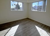 Thumbnail 11 of 21 - A room with wooden flooring and two windows showing a view of a street and buildings outside.