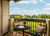Thumbnail 19 of 21 - A balcony with a table and chairs overlooking a green field.