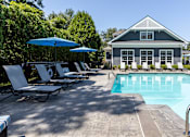 Thumbnail 2 of 19 - A pool area with lounge chairs and umbrellas in front of a house.